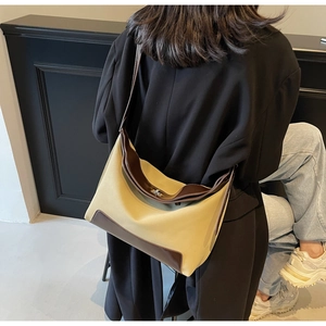 Detail of a large beige hobo bag with brown leather trim and silver clasp on a model