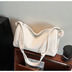Detail of white pleated shoulder bag with knotted strap and silver zipper on wooden shelf