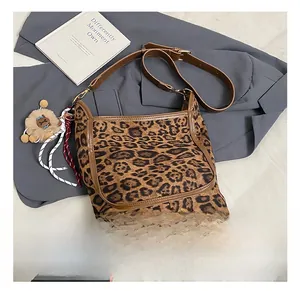 Detail of leopard print bucket bag with brown strap and plush charm on a grey suit background