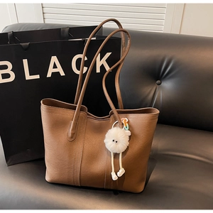 Close-up of brown faux leather tote bag texture with plush monster charm and zipper detail