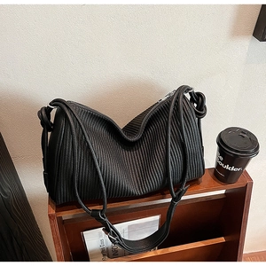 Detailed close-up of a black pleated leather tote bag with a rope strap on wood stairs