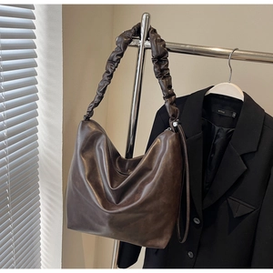 Detail of dark brown hobo bag featuring a gathered pleat shoulder strap and glossy texture