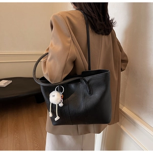 Detailed side view of black matte leather tote bag featuring a cute white plush monster charm
