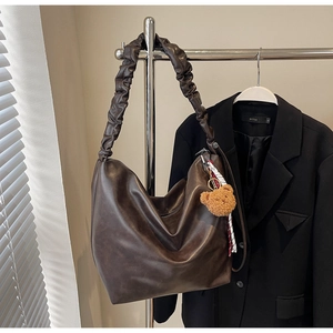 Detail of dark brown tote bag with ruffled shoulder strap and plush bear charm