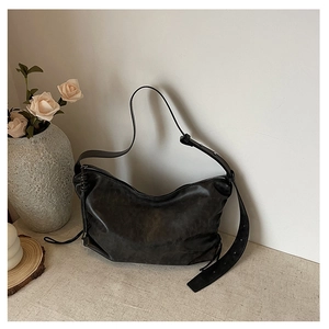 Detail of black leather crescent hobo bag with adjustable strap on a neutral table