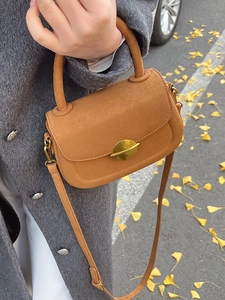 Brown suede crossbody saddle bag with gold buckle shown in autumn street setting