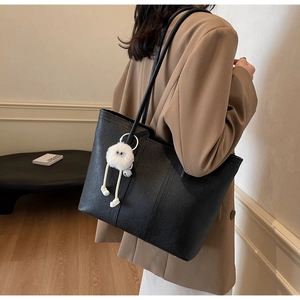 Detail view of large black tote bag with slender straps and a cute plush doll pendant