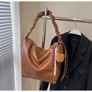 Detail of a brown retro hobo bag with pleated strap and a cute plush bear charm