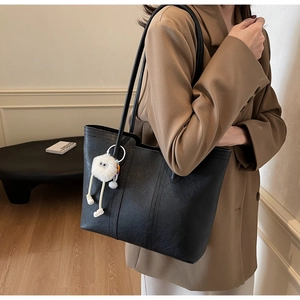 Detail of black lychee-grain leather tote bag with a cute plush doll charm on strap