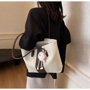 Detailed side view of a cream and brown tote bag with plush charm on a model's shoulder