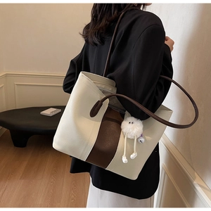 Detail of a large color-block tote bag with a plush charm worn on the shoulder