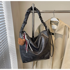 Detail of black matte leather shoulder bag with ruffled strap and bear charm accessory