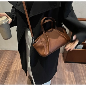 Brown leather crossbody pillow bag worn with a long coat in a minimalist interior