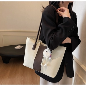 Detail of a large two-tone tote bag with plush charm accessory on a female model