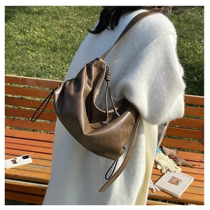 Detailed view of brown pleated crossbody bag with side knot accents and long shoulder strap