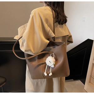 Brown leather tote bag with white plush monster charm shown in a minimalist setting