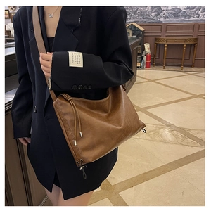 Detail of a dark brown pleated leather shoulder bag with drawstring accents and knotted strap