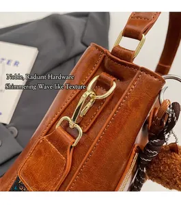 Detalle de bolso de cuero sintético marrón brillante con hebilla dorada y pompón
