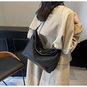 Detailed view of black nylon tote bag with silver buckle worn over a beige trench coat