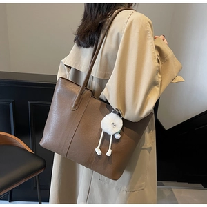 Detail of a brown faux leather tote bag with white fluffy charm on a female model
