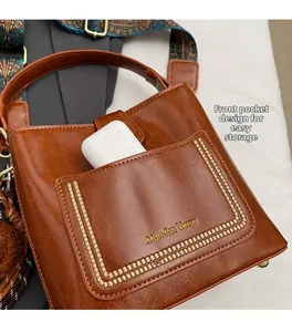 Detalle de bolso tipo cubo de cuero PU marrón con bolsillo frontal y correa étnica