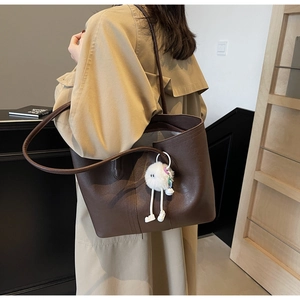 Close-up of a large brown tote bag featuring a cute white plush doll pendant for daily commute
