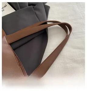 Close-up of brown pebbled leather tote bag showing handle craftsmanship and button closure