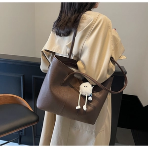 Detail of a large brown leather tote bag with soft plush monster charm on handle