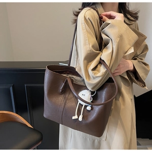 Detail of dark brown leather tote bag with plush monster charm on model beige coat