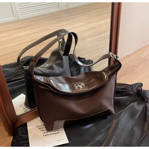 Detail of a brown matte leather shoulder bag featuring a silver metal twist lock and wide strap