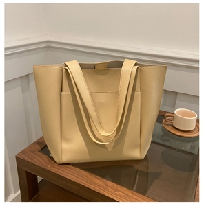 Detail view of large beige faux leather tote bag with front pocket on a coffee table