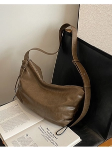 Brown vintage leather hobo bag with wide shoulder strap displayed on a chair