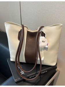 Large capacity bicolor tote bag in cream and brown with fuzzy charm on a sofa