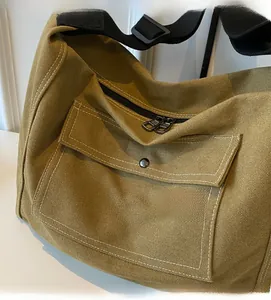 Detail of khaki canvas messenger bag featuring a front pocket and durable black zippers