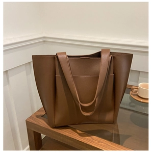 Close-up of brown litchi pattern leather tote bag with front pocket on a wooden table