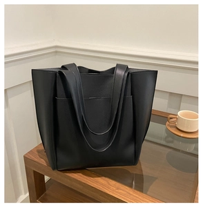 Detail of minimalist black leather tote bag with large capacity and functional front pocket