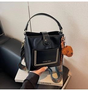 Detail der schwarzen Leder-Beuteltasche mit Goldlogo, Metallnieten und Plüschbär-Anhänger