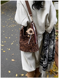 Detail of leopard print tote bag with plush charm and brown leather strap in autumn setting