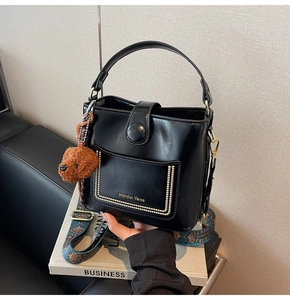 Detail der schwarzen Leder-Eimertasche mit Boho-Gurt und Plüschbär-Anhänger-Dekoration