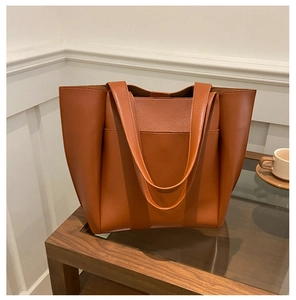 Detail view of a large caramel leather tote bag on a coffee table in a minimalist room