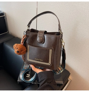 Detailansicht der dunkelbraunen Eimertasche mit bedrucktem Schultergurt und Bären-Anhänger