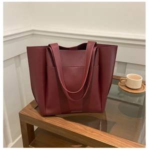 Detail shot of a large burgundy PU leather tote bag with front pocket on a coffee table