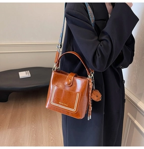 Detail der karamellfarbenen Eimertasche mit bedrucktem Schultergurt und Bärenanhänger
