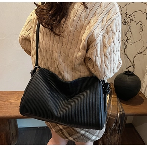 Detailed view of black textured leather bag with vertical stripes and wide shoulder strap