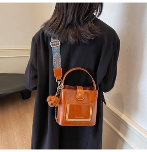 Braune Eimer-Ledertasche mit gemustertem breitem Gurt und Plüschbär-Anhänger Detail