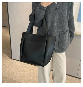 Detail of a black leather tote bag with a front pocket shown on a model for daily use