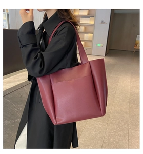 Detail view of large burgundy faux leather tote bag with front pocket on black trench coat