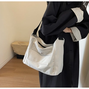 Canvas messenger bag in ivory white featuring a black wide strap and front flap pocket detail