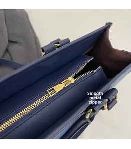 Detail of smooth golden hardware zipper on deep blue leather tote with brown lining