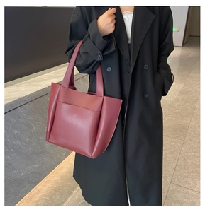 Burgundy leather tote bag with external pocket shown on shoulder with black coat
